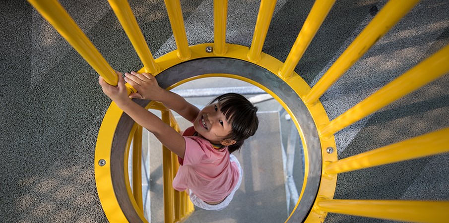 一个年轻的女孩在垂直梯子上爬上以糖厂为主题的游戏结构时对相机微笑。