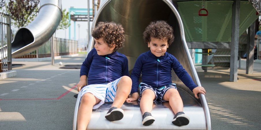 年轻的双胞胎男孩坐在多米诺公园离心机游乐场结构的不锈钢滑动底部。