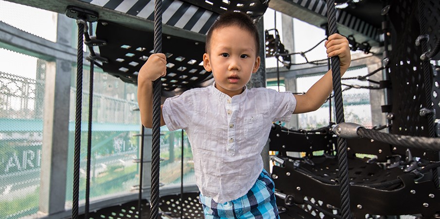 小男孩在Domino Park的Sweetwater Silo Playground结构内看着相机时握住货物网绳。