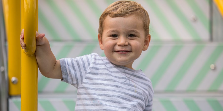 小男孩站在多米诺公园的游乐场台阶上时微笑。