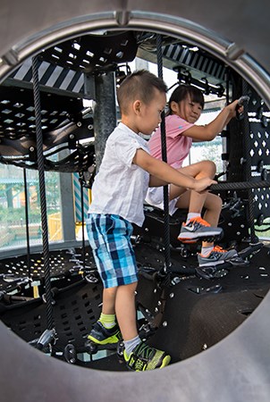 一个男孩和女孩在腰带货运网登山者的甜水筒仓游乐场结构内玩耍。