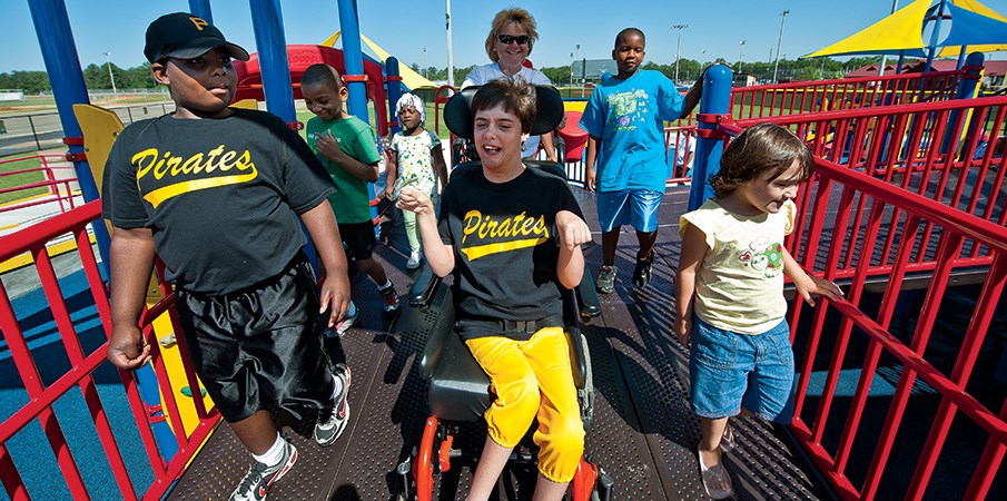 男孩在轮椅上微笑，一边与一群孩子一起骑着一个包容性的游戏机游乐场。足彩必威