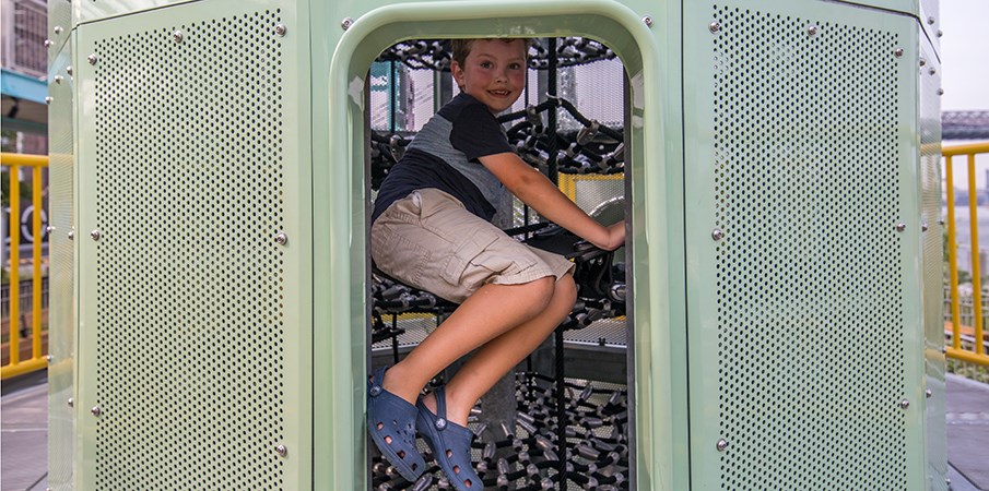 一个小男孩在离心机游乐场结构货运网登山者内攀登。