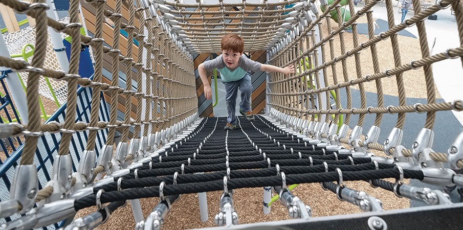 一个男孩爬上一个广场操场上的货物网隧道。