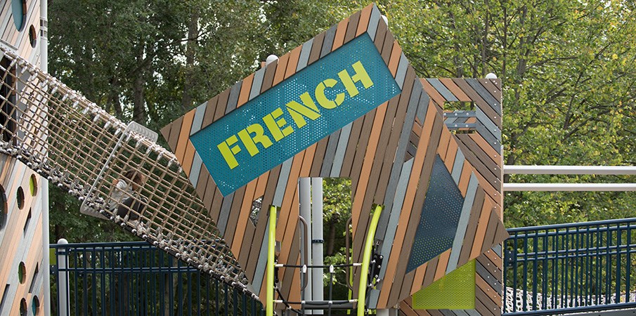 货网隧道连接着两个游戏结构，由真实和回收的塑料木材混合制成，上面有一个写着法语的标志。