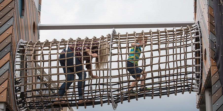 一个女人和一个男孩爬过一个高架游乐场的货物网隧道。