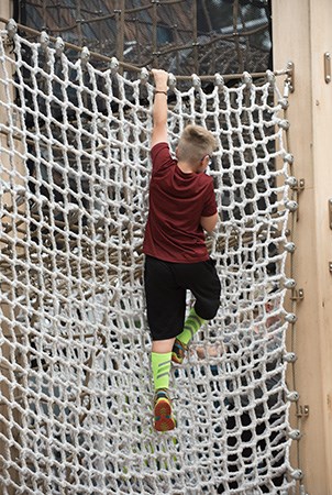 在操场上，一个男孩正在攀爬垂直吊货网。